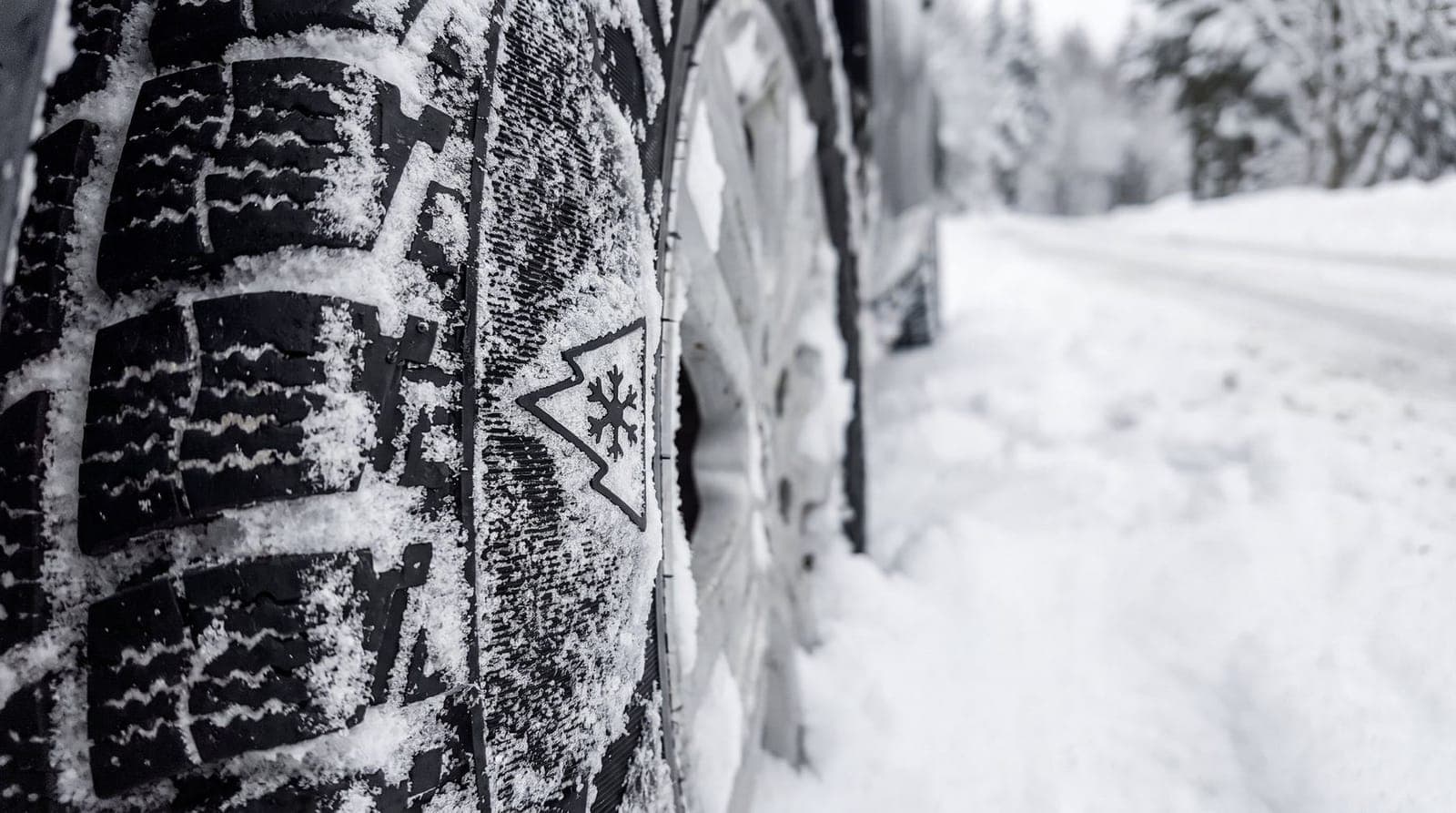 Flanc d'un pneu avec le pictogramme 3PMSF, roue posée dans la neige au bord d'une route de montagne