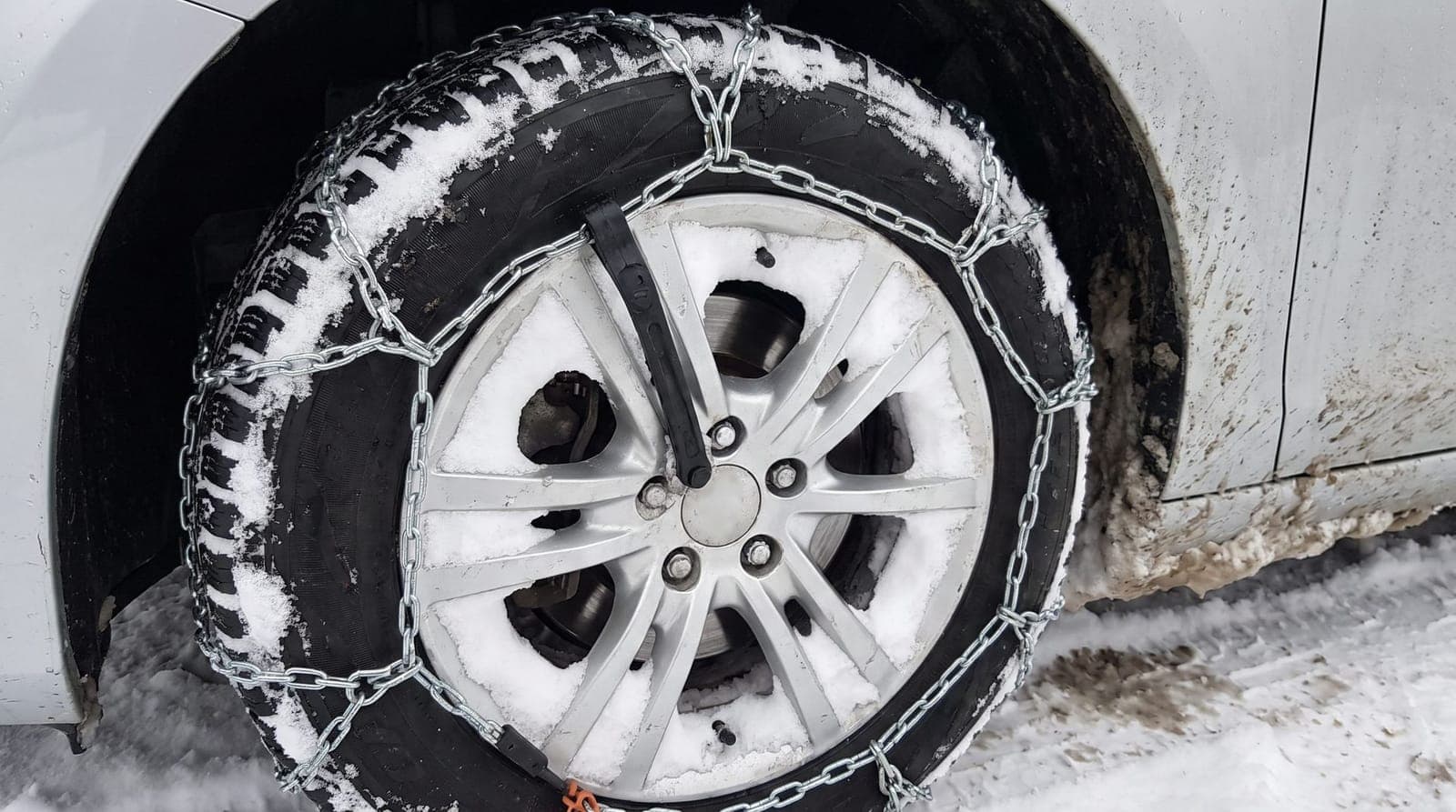 Gros plan sur une chaîne à neige montée sur une roue avant de voiture, dans un parking enneigé de montagne