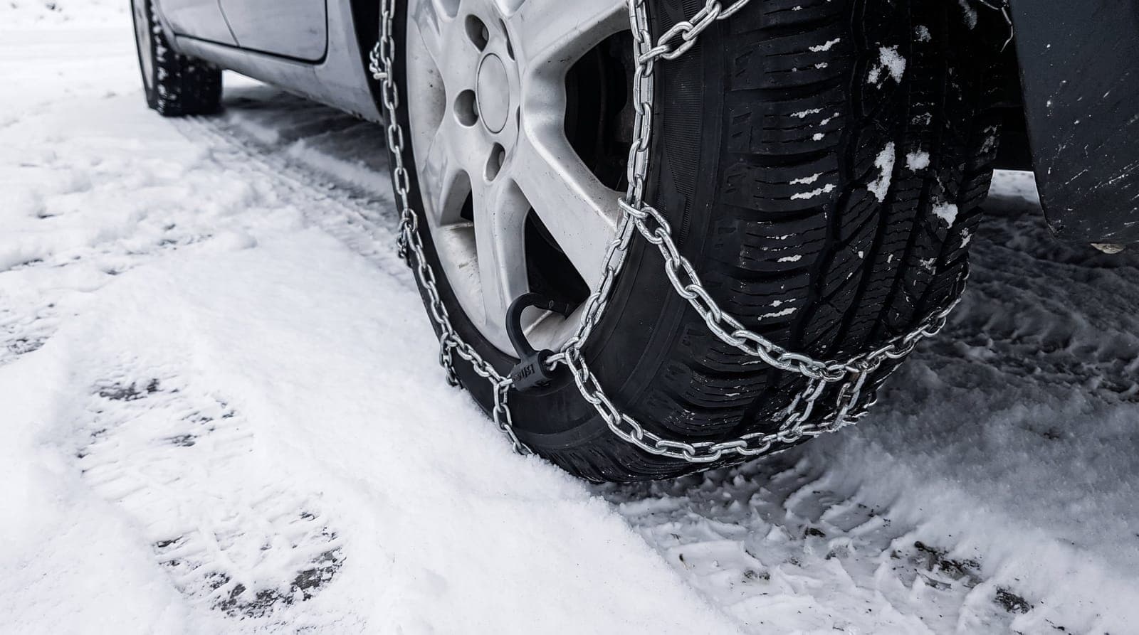 Chaîne à neige métallique montée sur le pneu avant d'une voiture, sur un parking enneigé de montagne
